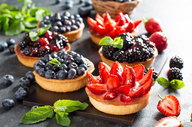 Tartaletas de fresas, arándanos, moras con ganache de chocolate, bayas frescas y hojas de menta, enfoque selectivo. Tarta de frutas frescas, tarta de frutas recién hecha en casa sobre una mesa