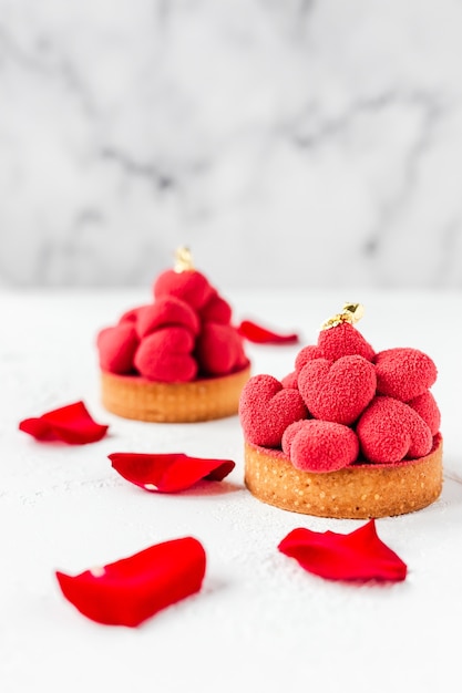 Tartaletas de postre dulce con corazones de mousse rojo en la parte superior, decoradas con pétalos de rosas rojas