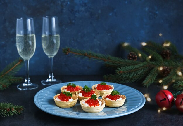Tartaletas con queso crema y caviar rojo en un hermoso plato en la mesa de Navidad.