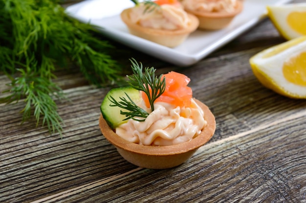 Tartaletas con queso crema y salmón salado sobre un fondo de madera. Sabroso tentempié ligero para una fiesta. Comer con los dedos.