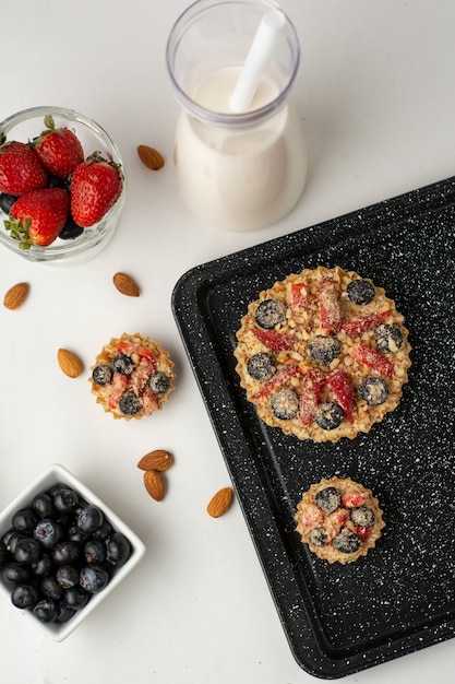 Tartaletas rellenas de crema pastelera y frutas y nueces en diferentes ángulos con fondo blanco.