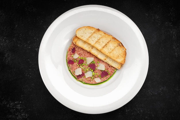 Tartar de carne con cebollas verdes y tostadas de pan en un plato