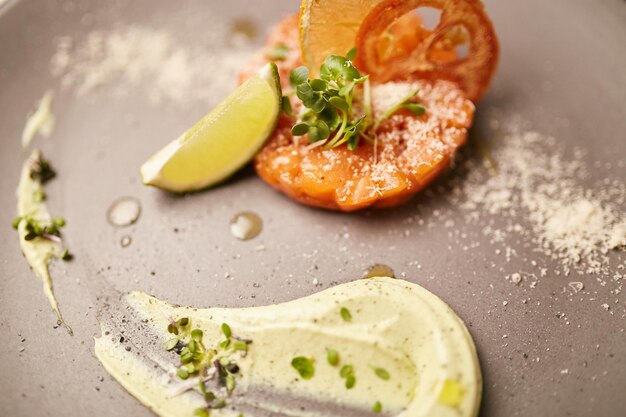 Tartar mit Kräutern Zitronenblütenblättern und Sauce auf einem grauen Teller