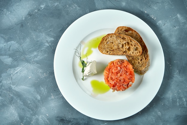 Tartar de salmón y aguacate, picatostes en una placa blanca sobre hormigón