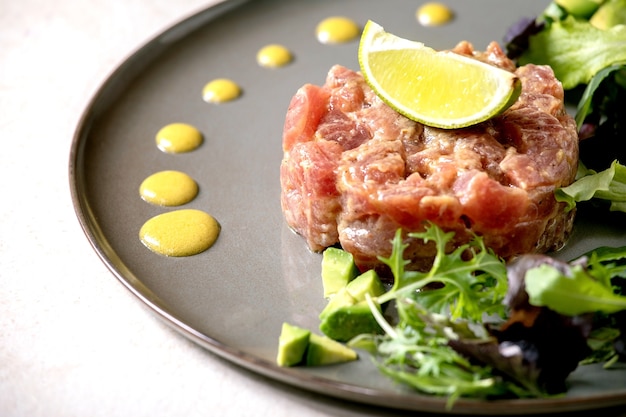 Tártaro de atum com salada verde, limão, abacate e molho de mostarda servindo em prato de cerâmica. jantar requintado, aperitivo de restaurante