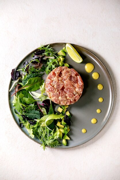 Tártaro de atum com salada verde, limão, abacate e molho de mostarda servindo em prato de cerâmica. Postura plana, copie o espaço. Jantar requintado, aperitivo de restaurante