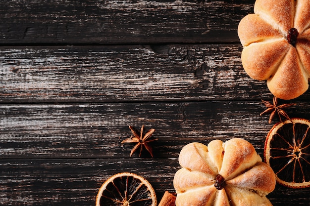 Tartas caseras en forma de calabaza y naranjas secas en madera oscura, vista superior con espacio de copia