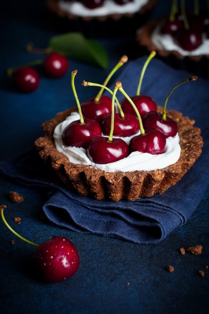 Tartas de chocolate con crema y bayas frescas de cereza dulce sobre una mesa de hormigón oscuro. Enfoque selectivo.