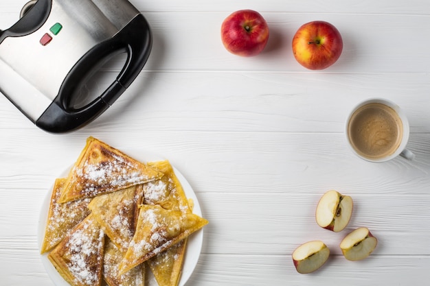 Las tartas se encuentran en la mesa junto a las manzanas, una tostadora y una taza de café.