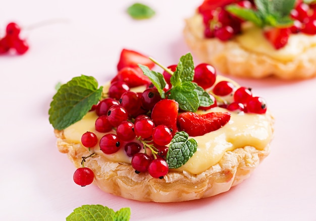 Tartas con fresas, grosellas y crema batida decoradas con hojas de menta.