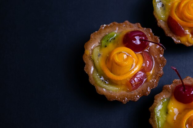 Tartas de frutas caseras con kiwi naranja y cereza sobre negro