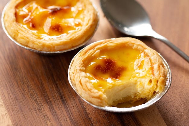 Tartas de huevo en taza de papel de aluminio en la mesa de madera, postre portugués tradicional servido en la cafetería