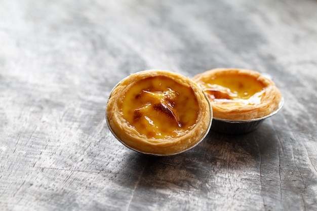 Tartas de huevo en una taza de papel aluminio en una mesa de madera, postre tradicional portugués servido en una cafetería