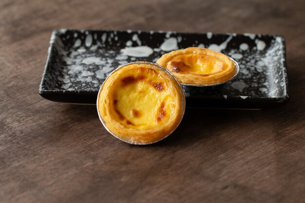 Tartas de huevo en una taza de papel aluminio en una mesa de madera, postre tradicional portugués servido en una cafetería