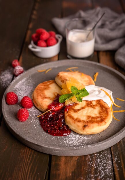 Tartas de queso panqueques de cuajada con mermelada de frambuesa y crema agria en una vista lateral de la placa gris