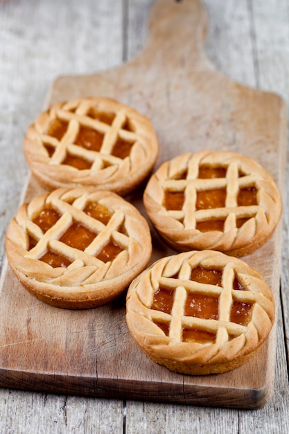 Tartas recién horneadas con mermelada de mermelada o albaricoque que se llenan en la tabla de cortar en la rústica mesa de madera.