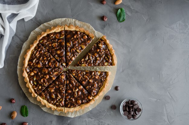 Tarte com caramelo de chocolate, avelãs, amendoins, amêndoas e mistura de sementes em um fundo de concreto escuro. Orientação horizontal. Vista do topo. Copie o espaço.