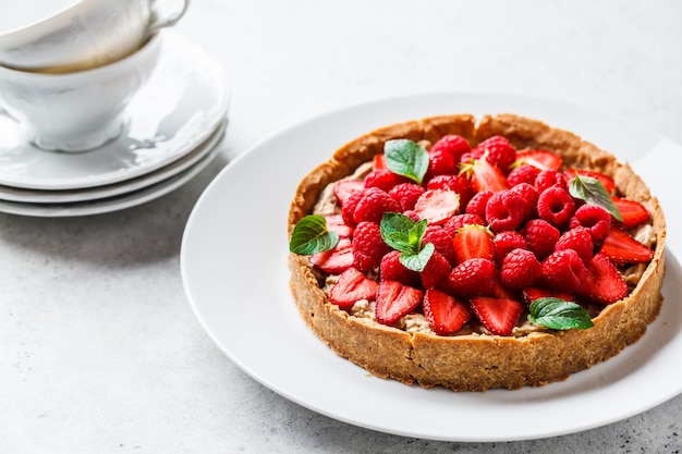 Tarte de bagas inteiro com framboesas, morangos e creme no prato branco