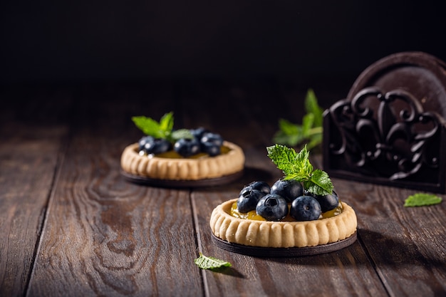 Tartelete de shortbread caseiro com coalhada de limão e mirtilos frescos na velha superfície de madeira escura. Conceito de comida de férias com espaço de cópia