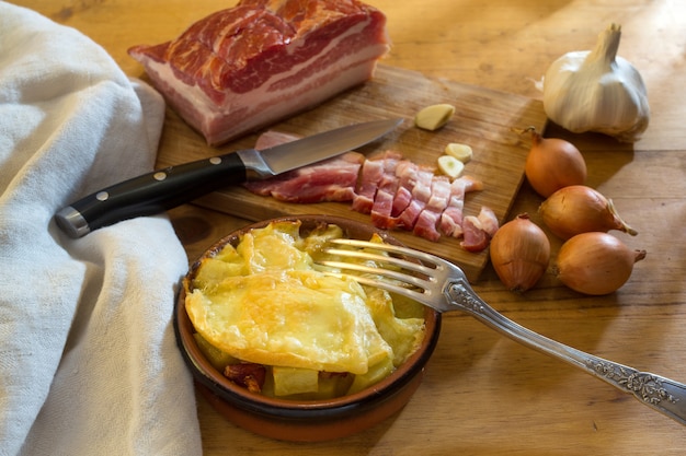 Tartiflette pequena, ao lado da tábua com barriga de porco