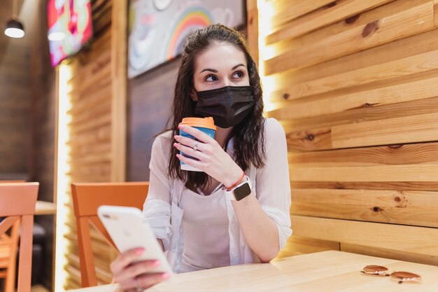 Tasa de cuarentena en un café, una mujer joven con una máscara negra. Foto de alta calidad