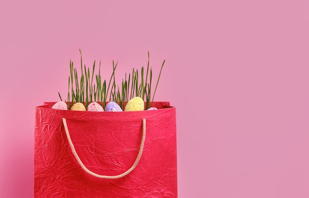 Tasche mit Gras Ostereiern auf rosa Hintergrund