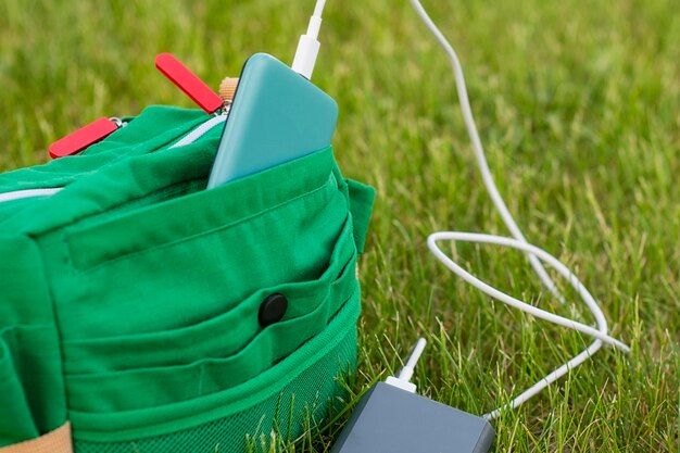 Tasche mit Smartphone wird über eine Powerbank aufgeladen. Tragbares Ladegerät in der Natur und auf Reisen