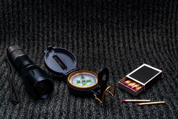 Taschenlampe, Kompass, Streichhölzer auf grauem Stoffhintergrund