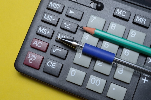 Taschenrechner Bleistift und Kugelschreiber auf gelbem Grund. Nahaufnahme.