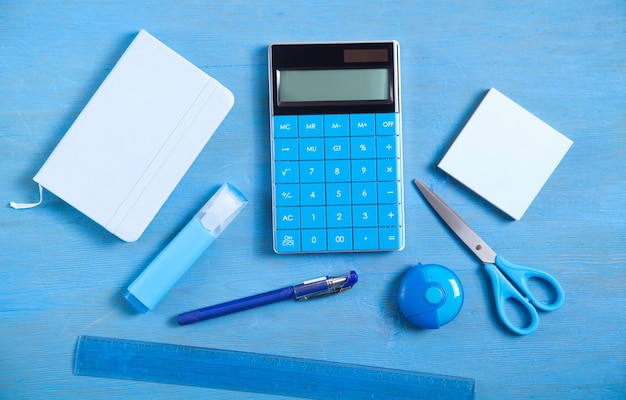 Taschenrechner, Notiz, Radierschere, Stift, Marker, Haftnotizen auf der blauen Oberfläche.