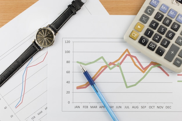 Taschenrechnerarmbanduhr und blauer Stift auf Diagrammhintergrund.