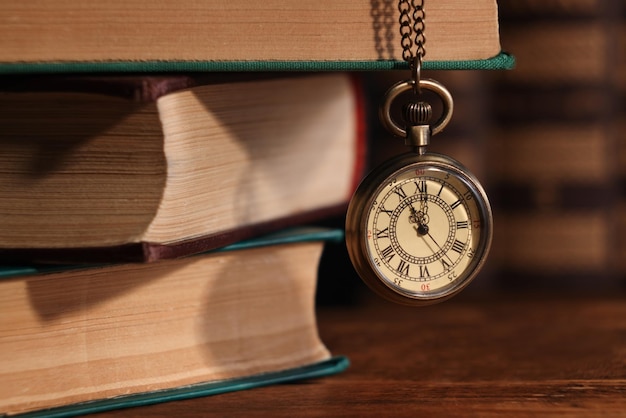 Taschenuhr hängt auf einem Stapel Bücher an einem Holztisch