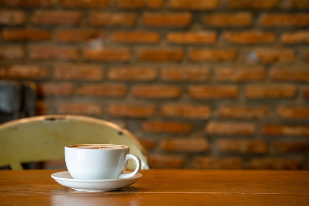 Tasse Cappuccino auf Holztisch gegen Ziegelsteinwand im Innenbereich