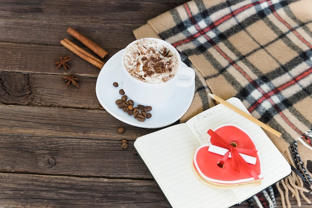 Tasse Cappuccino, herzförmige Kekse Breite Nachricht, Notizbuch und kariertes Plaid auf einem braunen Holztisch