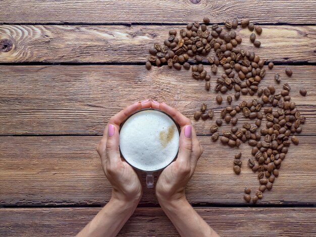 Tasse Cappuccino in der Hand. Kaffeebohnen auf dem hölzernen Hintergrund