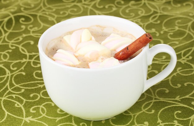 Tasse Cappuccino mit Marshmallows und Zimt auf grüner Tischdecke