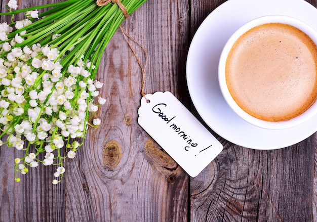 Tasse Cappuccino und ein Bouquet von weißen Maiglöckchen
