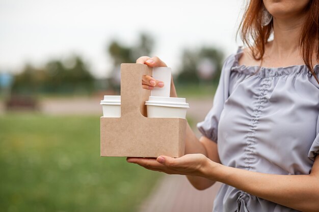 Tasse des weißen Papiers zwei mit Kaffee in der Frauenhand. Zeit zum Kaffeetrinken in der Stadt. Kaffee zum Mitnehmen. Genießen Sie den Moment, machen Sie eine Pause. Einweg-Pappbecher Nahaufnahme. Leckeres Heißgetränk. Leerzeichen für Text,