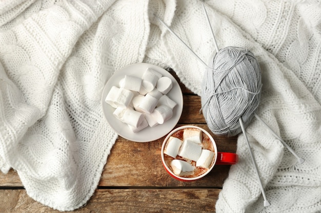 Tasse frischen Kaffee mit Marshmallow und gestricktem Plaid auf Holztisch, Draufsicht