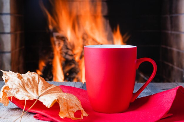 Tasse für Tee oder Kaffee und Herbstlaub vor gemütlichem Kamin