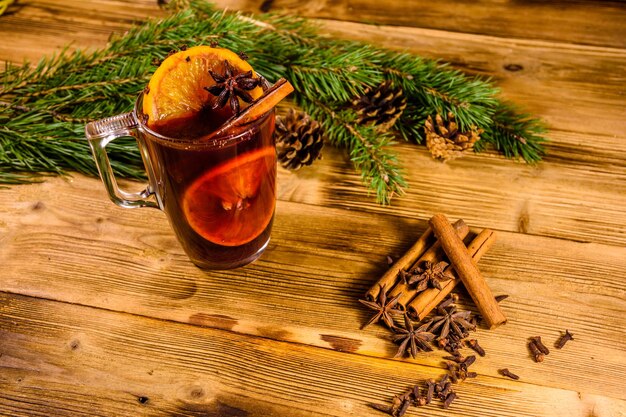 Tasse Glühwein mit Zimt- und Tannenzweigen auf rustikalem Holztisch