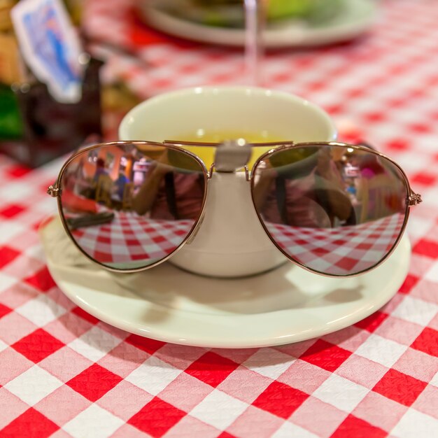 Tasse grüner Tee auf einer karierten Tischdecke und einer Sonnenbrille