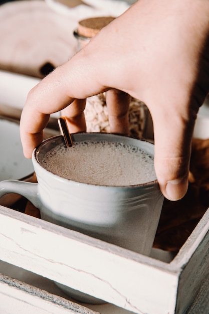 Tasse hafermilch mit einer hand, die sie packt, in launischen tönen in einer gemütlichen tasse