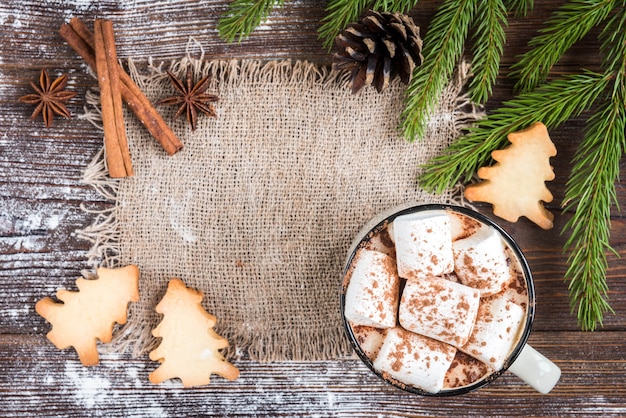 Tasse heiße Schokolade mit Marshmallow, Gewürzen, Weihnachts-Ingwerplätzchen, Tannenzweigen und Zapfen auf dunklem hölzernem Hintergrund. Kopieren Sie Platz für Text. Weihnachtstapete, Karte.