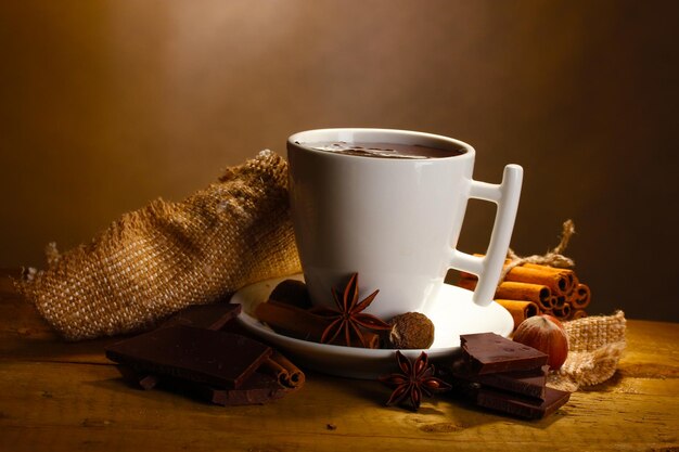 Tasse heiße Schokolade, Zimtstangen, Nüsse und Schokolade auf Holztisch auf braunem Hintergrund