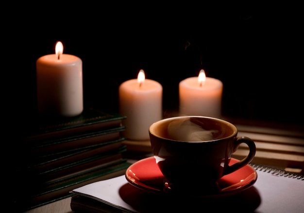 Tasse heißen Kaffee mit gelbem Rauchnotizbuch mit Bleistift und brennenden Kerzen Schreibtischtisch