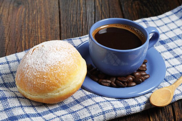 Tasse heißen Kaffee mit süßem Donut zum Frühstück auf dem Küchentisch