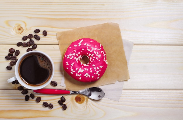 Tasse heißen Kaffee mit süßem Donut zum Frühstück auf Holztisch, Ansicht von oben