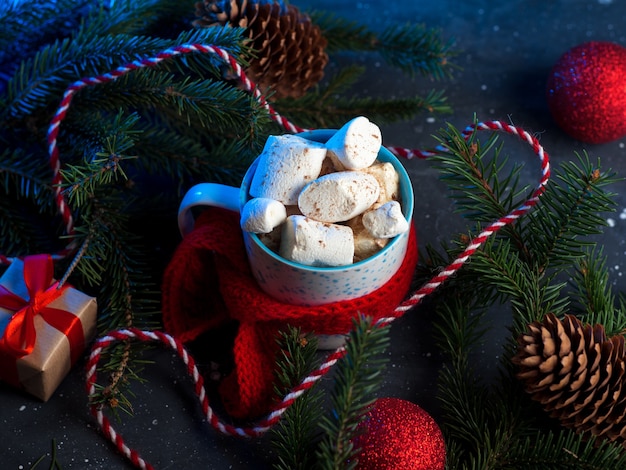 Tasse heißen Kaffee oder Schokolade mit Marshmallows, rotem Strickschal, Weihnachtsdekoration, Luftballons und Geschenken