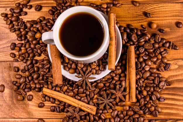 Tasse heißen Kaffee, Sternanis, Zimtstangen und verstreute Kaffeebohnen auf rustikalem Holztisch. Ansicht von oben